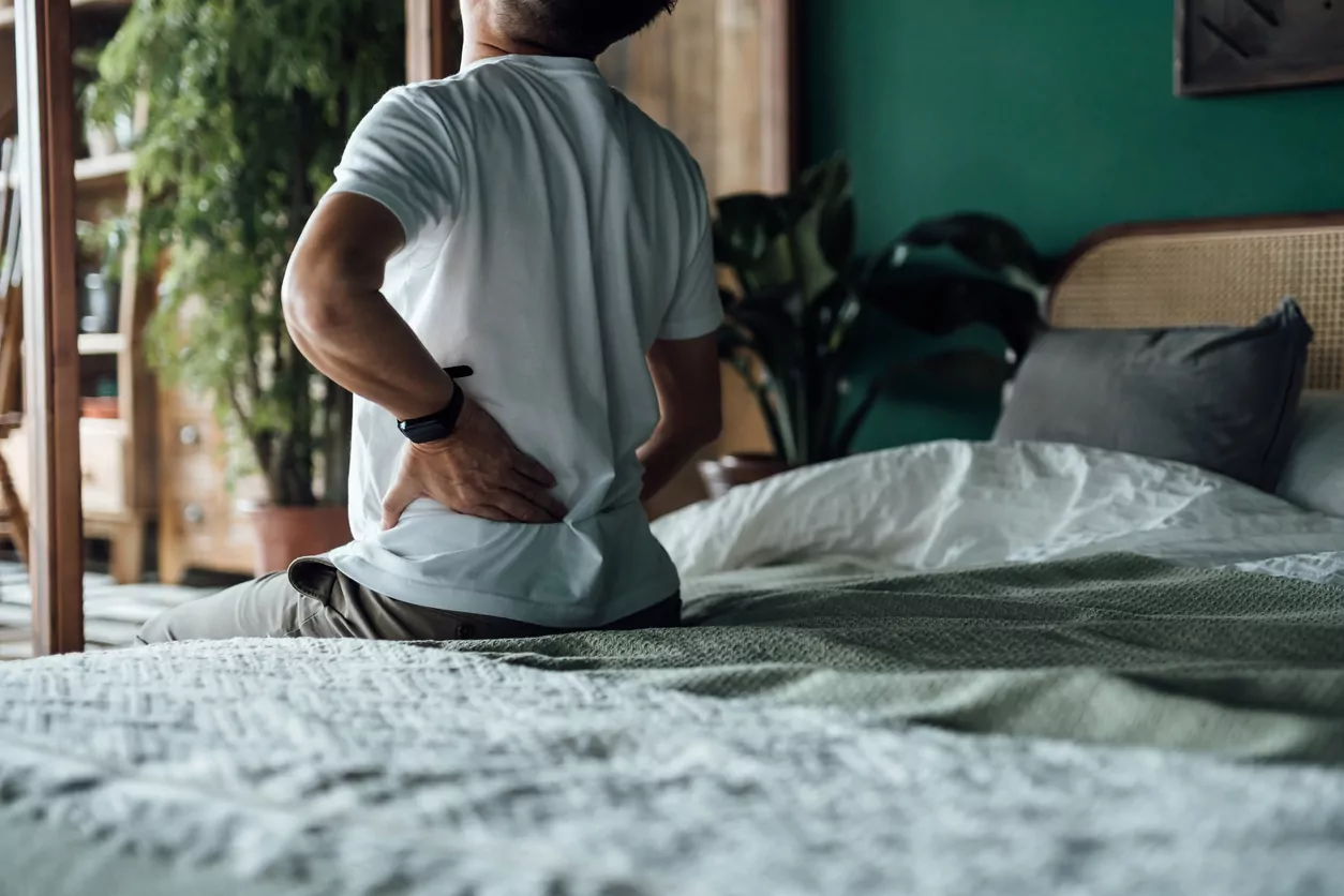 man bracing lower back on bed and considering physical therapy for lower back pain