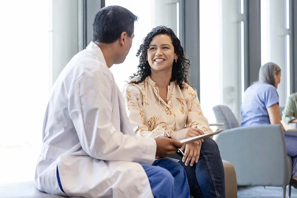 The young adult woman smiles broadly as she gets good news about her family member from the unrecognizable male surgeon.